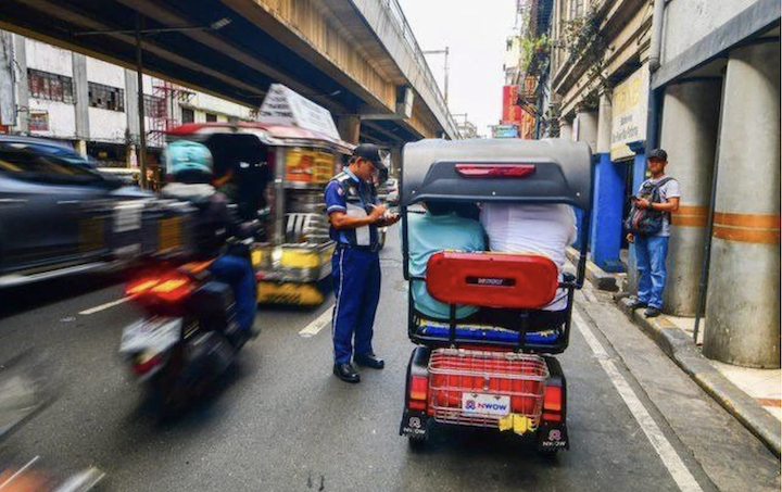 A traffic enforcer issues a violation ticket to an e-bike driver