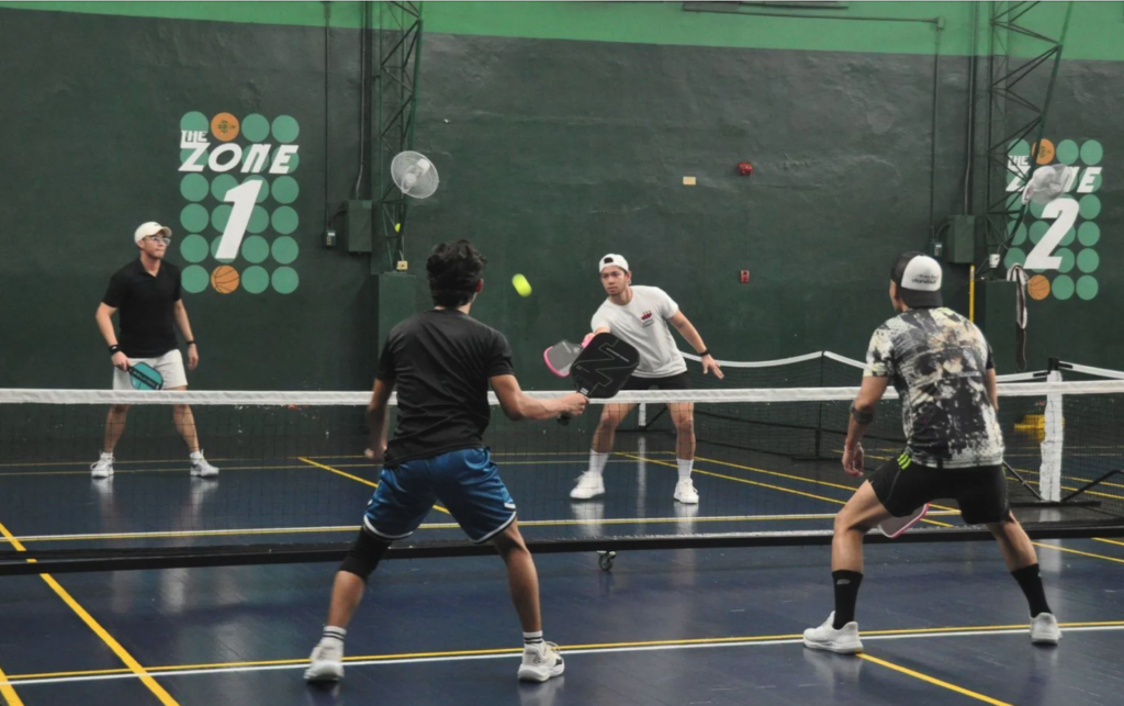 Four players engaged in a doubles pickleball match on an indoor court in Manila.