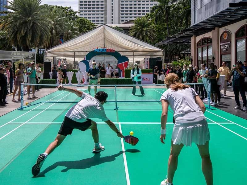 Players competing in an outdoor pickleball game during a public event in a city setting.